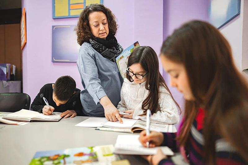 Teacher helping elementary school students while the work on an assignment.